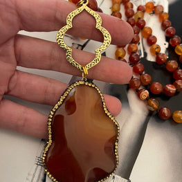 Collar Hippie Chic largo con preciosas piedras naturales rojas anaranjadas con colgante en los tonos y detalles de Pave dorados y negros.